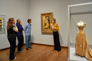 Museumbezoekers kijken naar het schilderij 'Avond (Het bal)' van James Tissot in de tentoonstelling 'Geel. Meer dan Van Goghs lievelingskleur'. In de vitrine naast het schilderij is de baljapon van geel fluweel te zien. Foto: Michael Floor