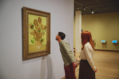 A young man looks intently at Van Gogh's Sunflowers in the Van Gogh Museum. He holds the hand of his girlfriend who is standing behind him. Photo: David Stegenga