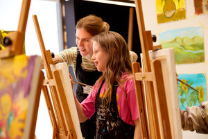 Een meisje is aan het schilderen in het atelier van het Van Gogh Museum terwijl de workshopdocente vriendelijk lachend meekijkt. Foto: Suzanne Karsters