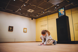 Een kind zit op de grond en doet de speurtocht bij de zelfportretten van Vincent van Gogh. Foto: Jelle Draper