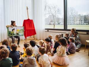 Een museumdocente laat een grote versie zien van het gouden boekje Vincent en Camille aan kleuters uit groep 1 en 2 tijdens de rondleiding Camille en kleur in het Van Gogh Museum. Foto: Jelle Draper