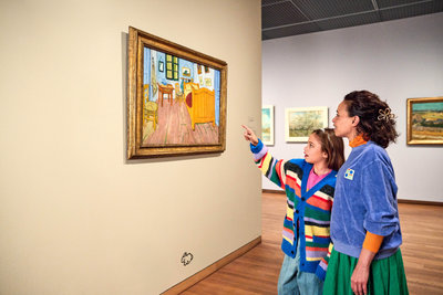 Een meisje wijst naar het schilderij De slaapkamer van Vincent van Gogh in het Van Gogh Museum. Haar moeder staat naast haar en kijkt mee. Foto Suzanne Karsters