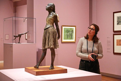 Een vrouw luistert naar de audiotour en kijkt naar het beeld Veertienjarig danseresje (Petit danseuse de quatorze ans) van Degas in de tentoonstelling Vive l'impressionnisme! in het Van Gogh Museum. Foto: Michael Floor